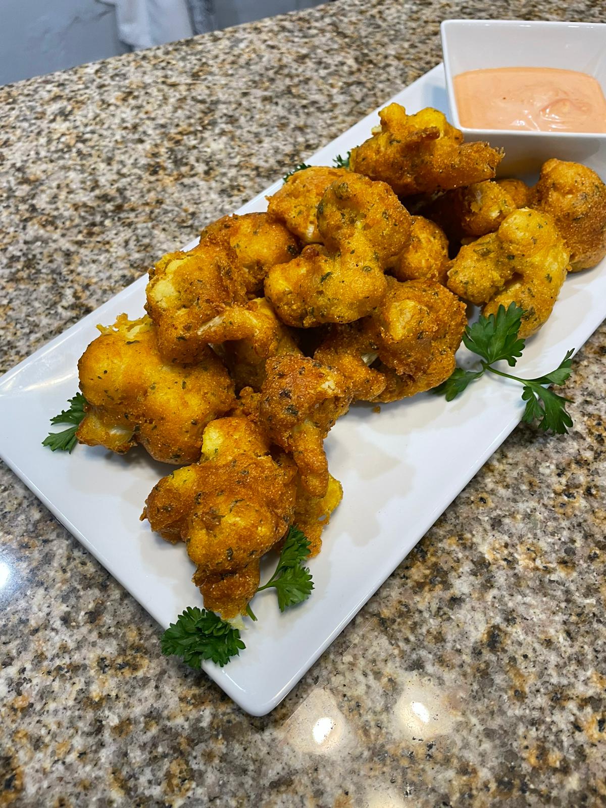 Battered cauliflower golden yellow in a rectangle white tray garnished with parsley on a marbled counter