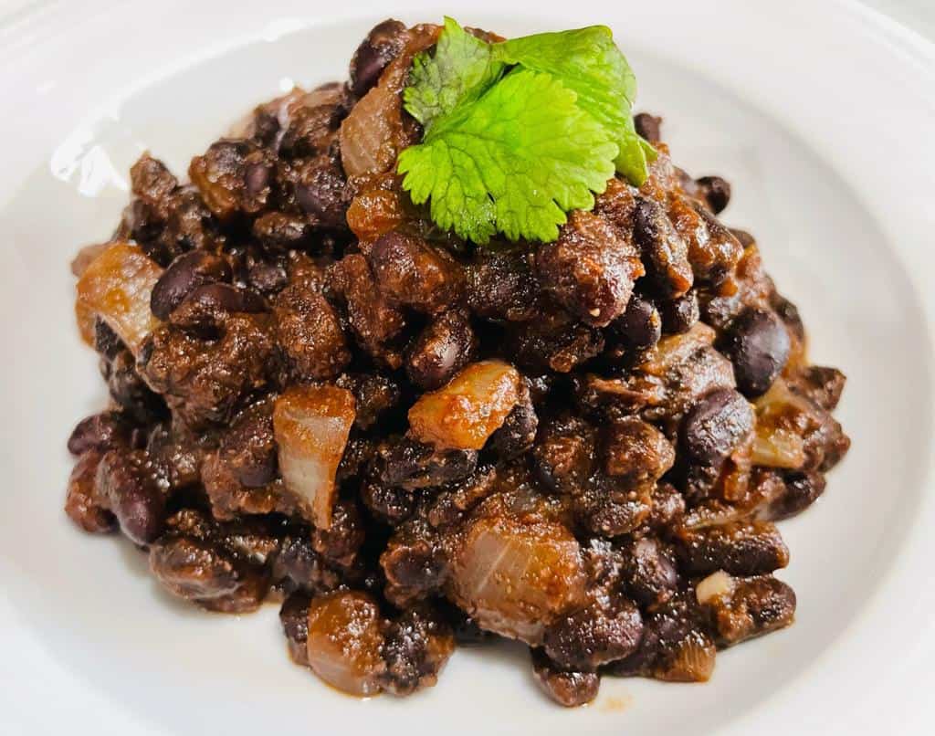black beans cooked and on a white plate with a piece of green cilantro leaf on top
