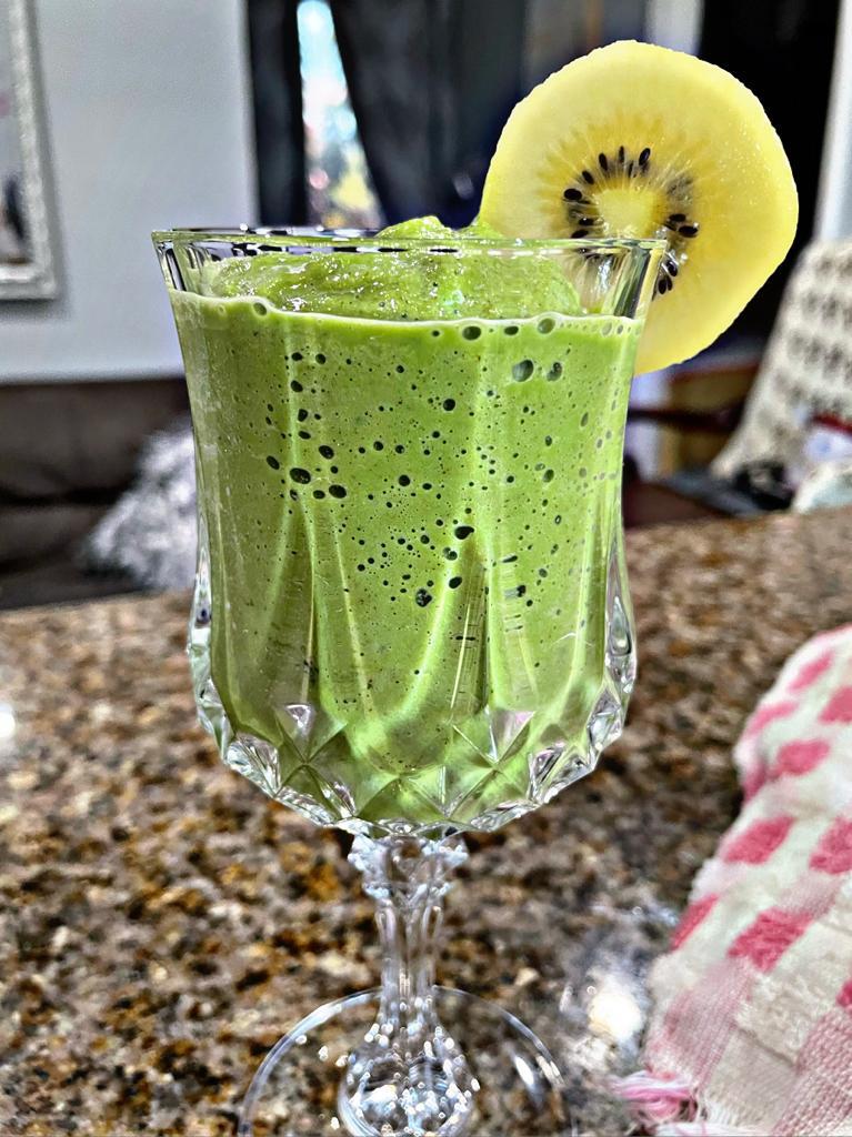 green smoothie with kiwi on the rim on a counter with a red kitchen towel