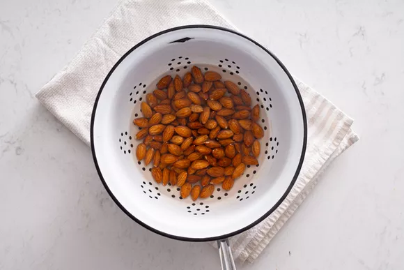 Almond nuts in a white strainer on a white towel, folded