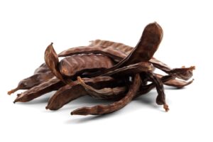 carob pods in a pile with a white background