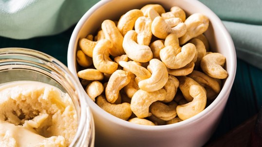 whole cashews in a white bowl with a cashew butter next to it