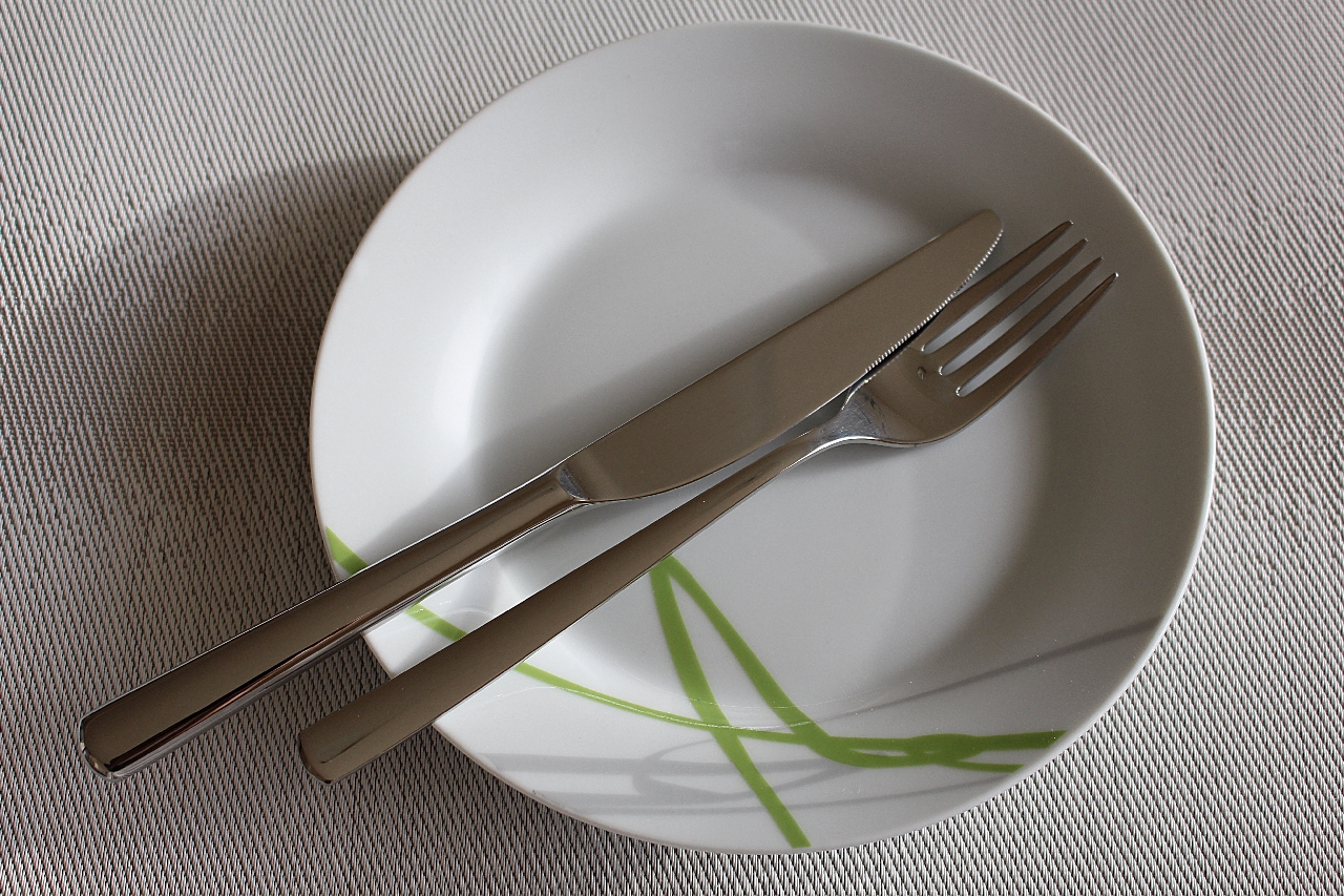 a white empty clean plate with a fork and knife in the middle on a white background