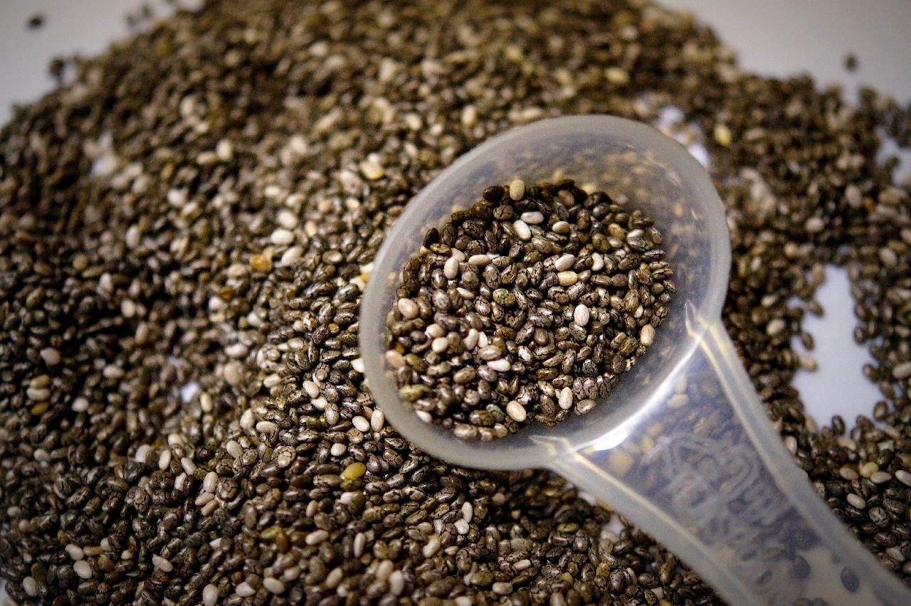 Black Chia seeds poured out onto a surface with a white plastic tablespoon almost full