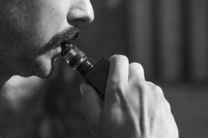 a man with a mouthstache with the vaping device in his moth
