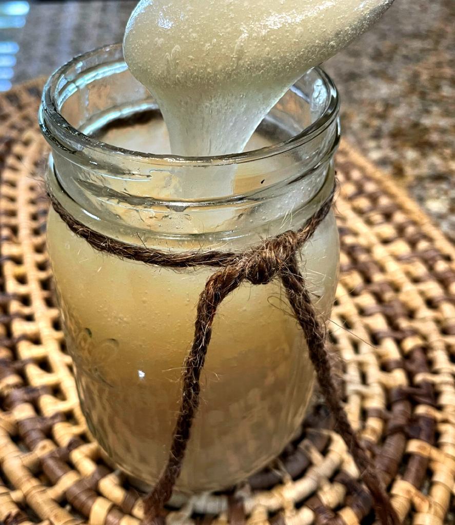 Sea moss gel in a balls jar with a spoon inside showing the smooth texture and on a weaved placemat