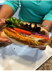 lady in a aqua blouse holding a sub burger with tomato slices sprouts and lettuce