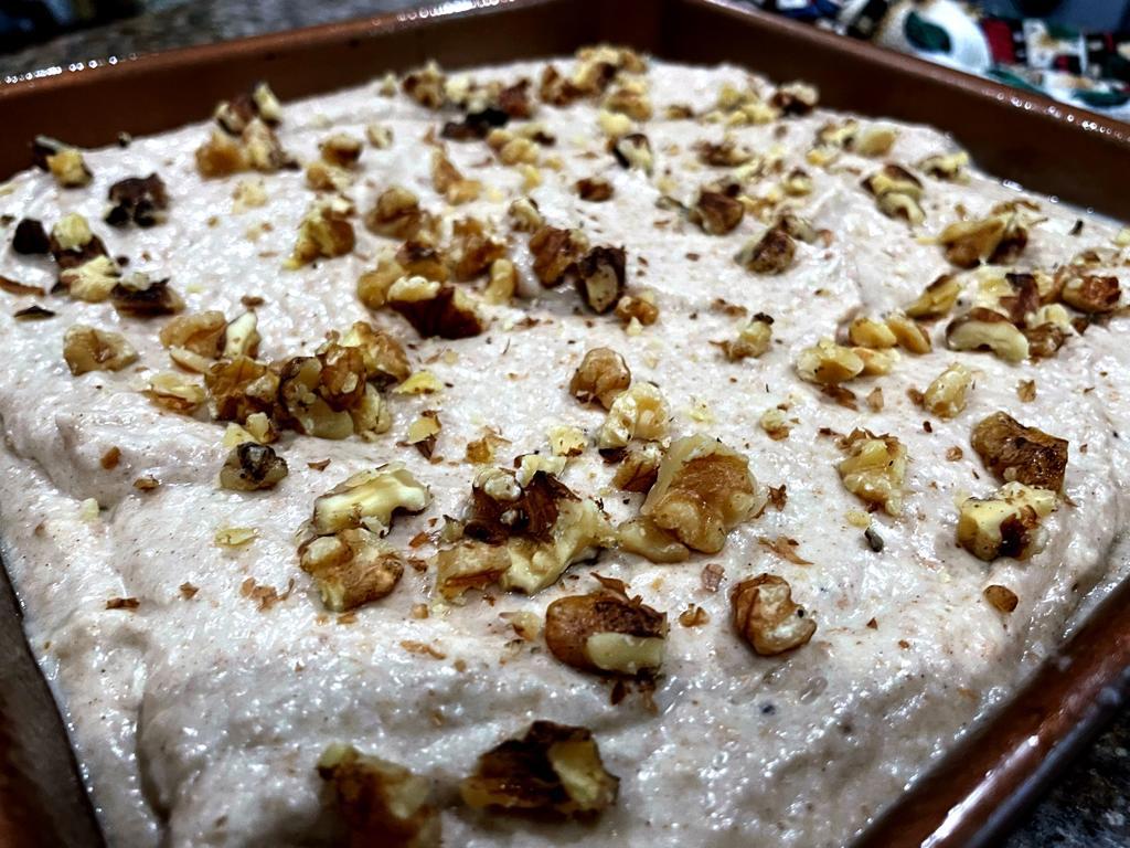 plantain bread in baking pan topped with broken pieces of walnuts on top