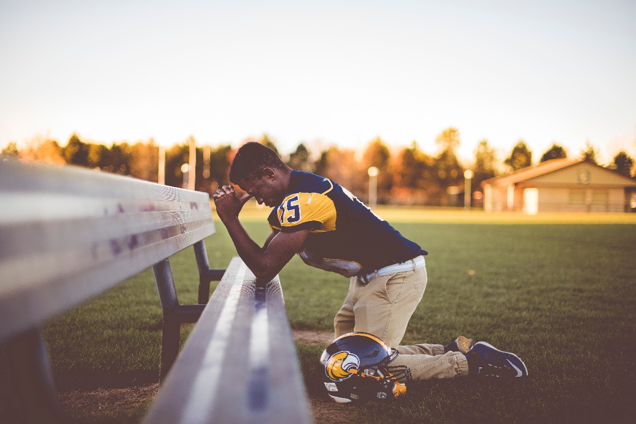 praying-in-football-uniform-on-his-knees on an open field