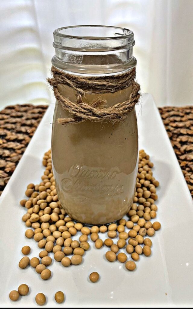 soy milk in a milk bottle on white tray with soy beans 