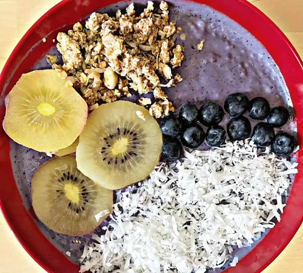 smoothie bowl with coconut shreads, blueberries, kiwi and granola on top on a red bowl