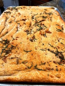 focaccia bread baked on a tray golden brown, with rosemary and garlic on top