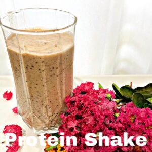 a clear glass of protein shake on a white glass with white background with fresh picked pink flowers laying near it