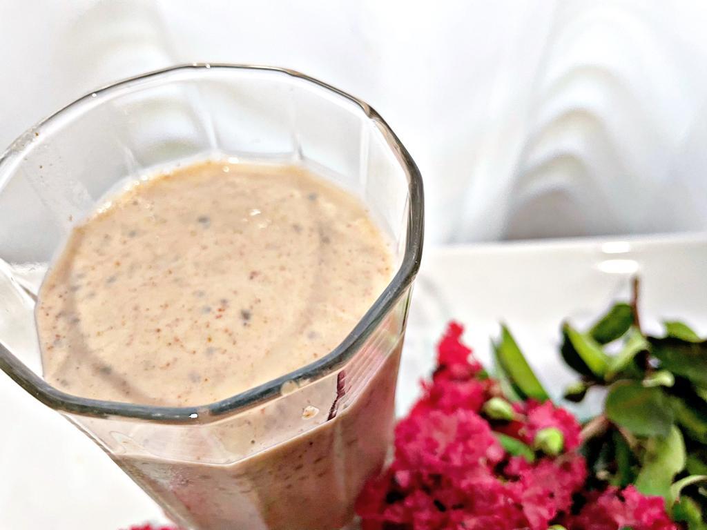 a drinking glass with the protein shake, chia, tofu and nut butter all blended, sitting on a white plate with pink flowers 