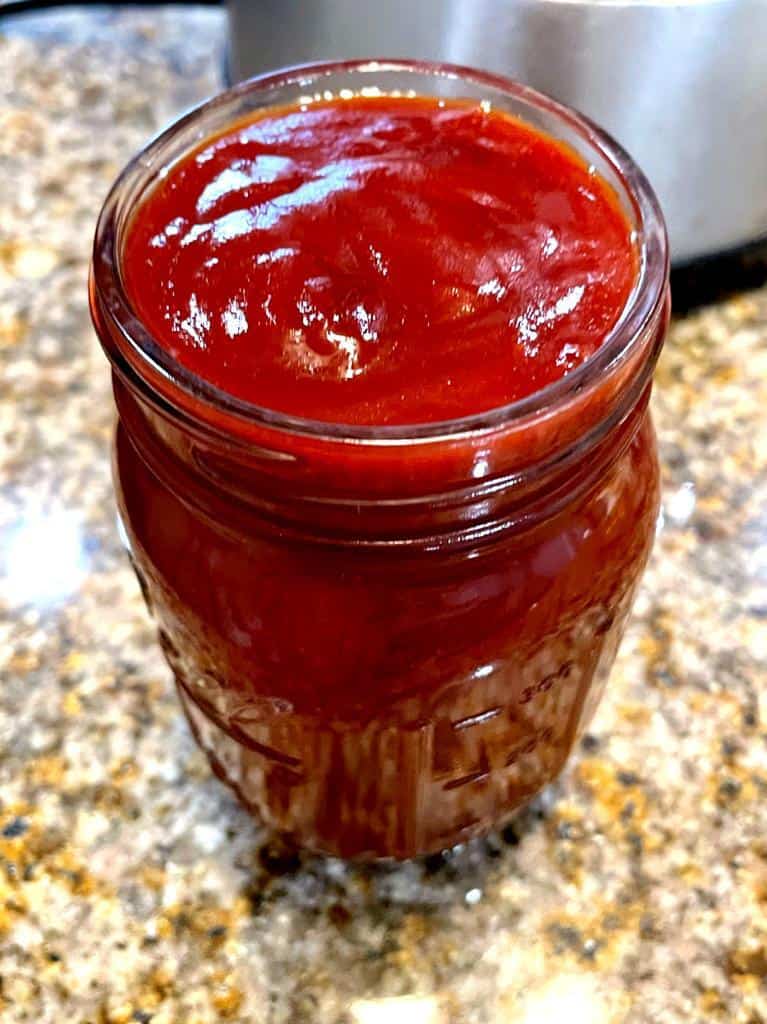 homemade bbq sauce, with ketchup, molasses, cumin, lemon juice, maple syrup. a balls jar filled with bbq sauce on a counter