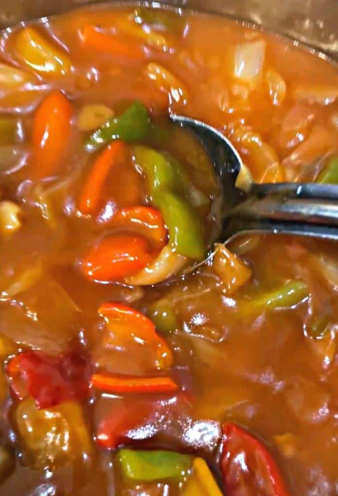 sweet and sour sauce with bell peppers, green and red, with onions in a spoon. 