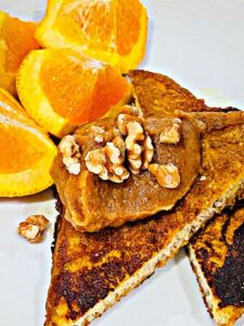 french toast pumpkin spice on a white plate with a few pieces of oranges and topped with date spread and walnuts