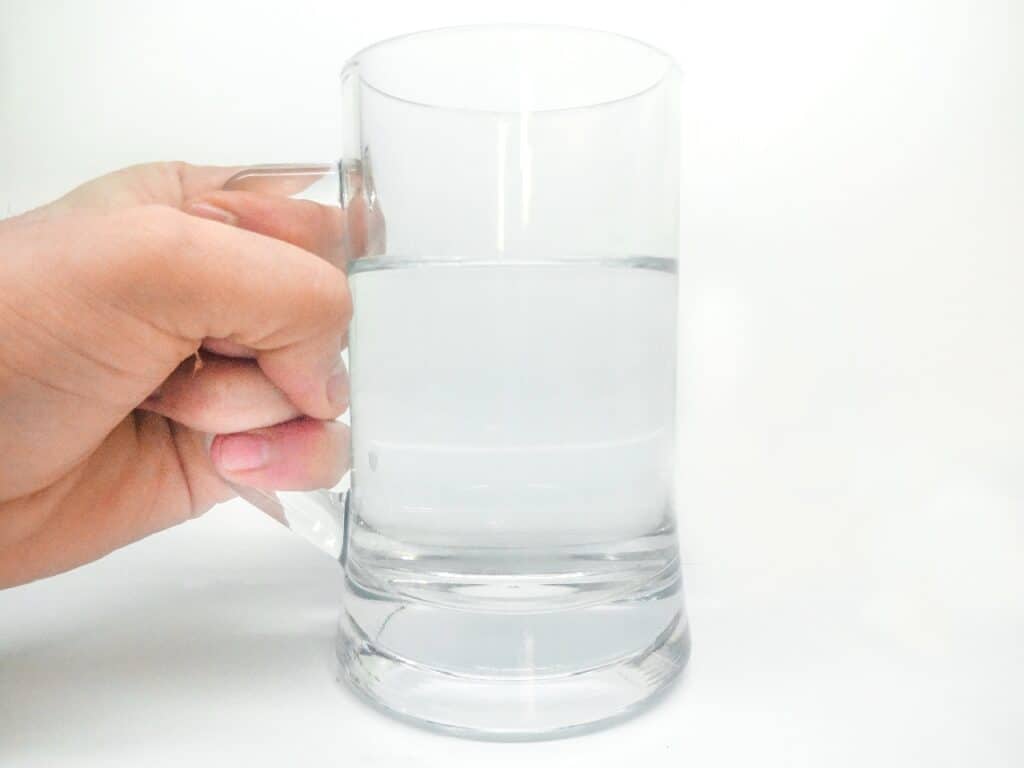 glass of water with a hand holding the hamdles on the glass handle