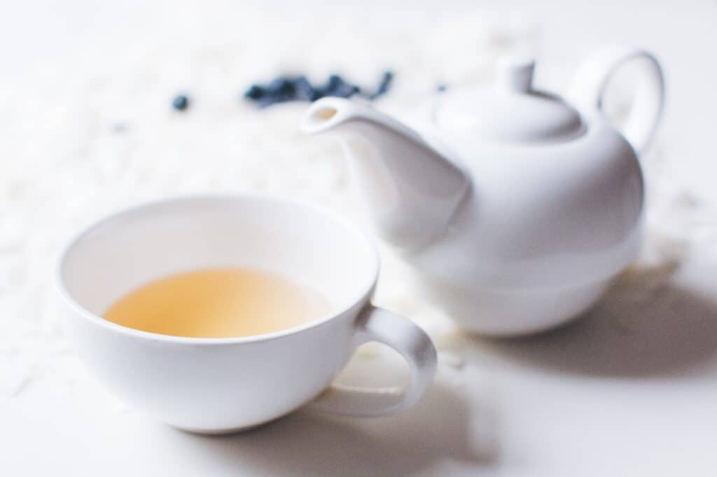 a white mug of tea with a white tea pot