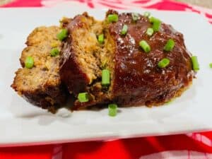Tofu Meatloaf on a white plate with green onions on top with BBQ sauce