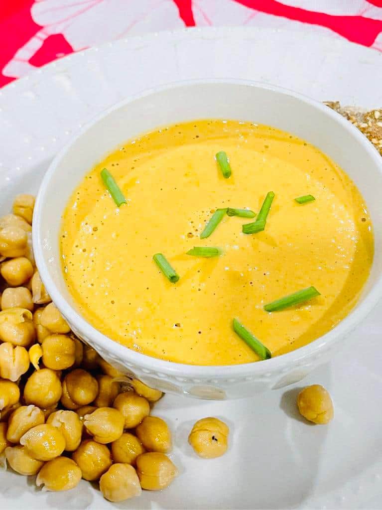garbanzo or chickpeas on a plate with a red background and a cheese sauce in a bowl with green onions chopped on top