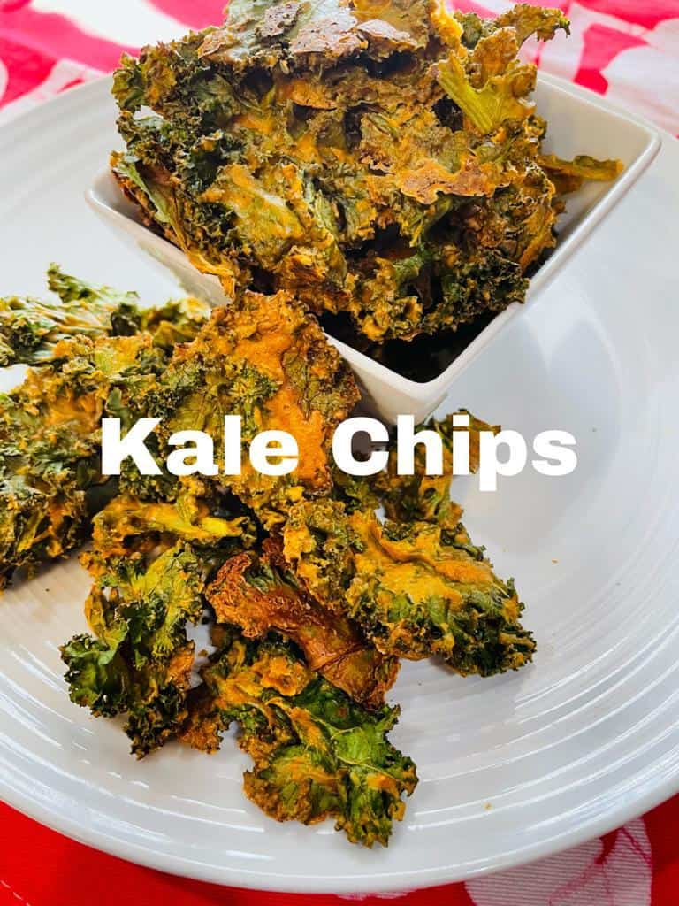 Kale chips on a white plate and some in a square bowl on top of the plate and a red and white background