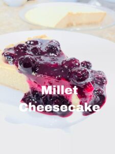 One slice of millet cheesecake with cooked blueberry sauce on top, white plate