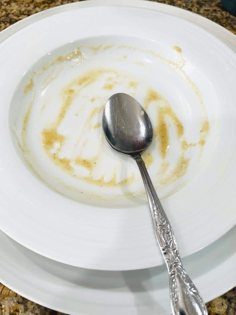 EMPTY WHITE BOWL WITH SPOON IN IT AND JUST SMALL BITS OF FOOD