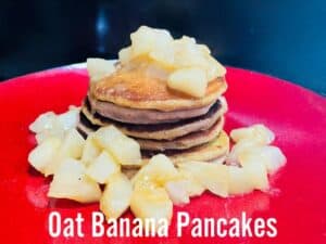 a red plate with a stack of banana oat pancakes on it topped with cooked pears
