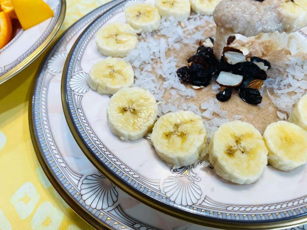 A BOWL OF PORRIDGE WITH BANANAS ON THE RIM AND RAISINS AND NUTS ON TOP