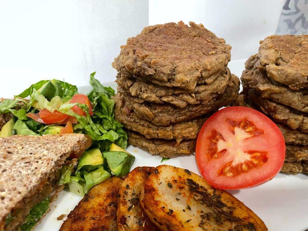 BUrgers stacked with green salad, tomato, avocado and slided potatoes 