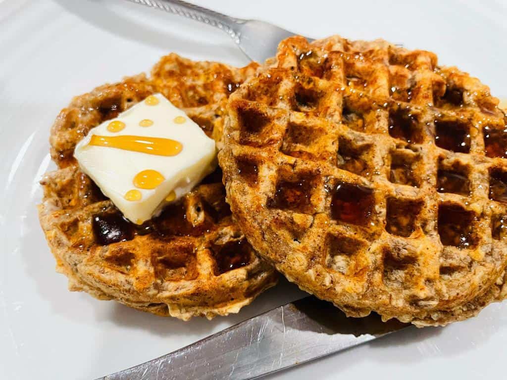 2 Waffles on a white plate with a pat of butter and a drizzle of syrup