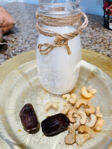 cashew milk in a milk jar with cashews and dates on a clear glass plate
