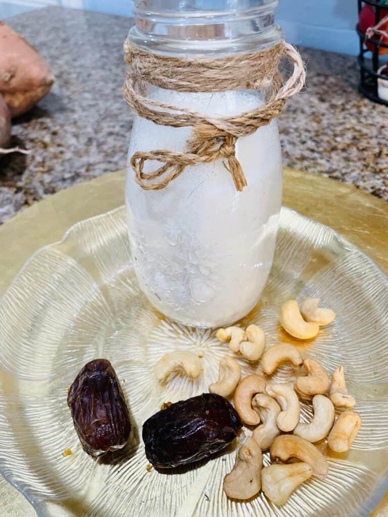 cashew milk in a milk jar with cashews and dates on a clear glass plate